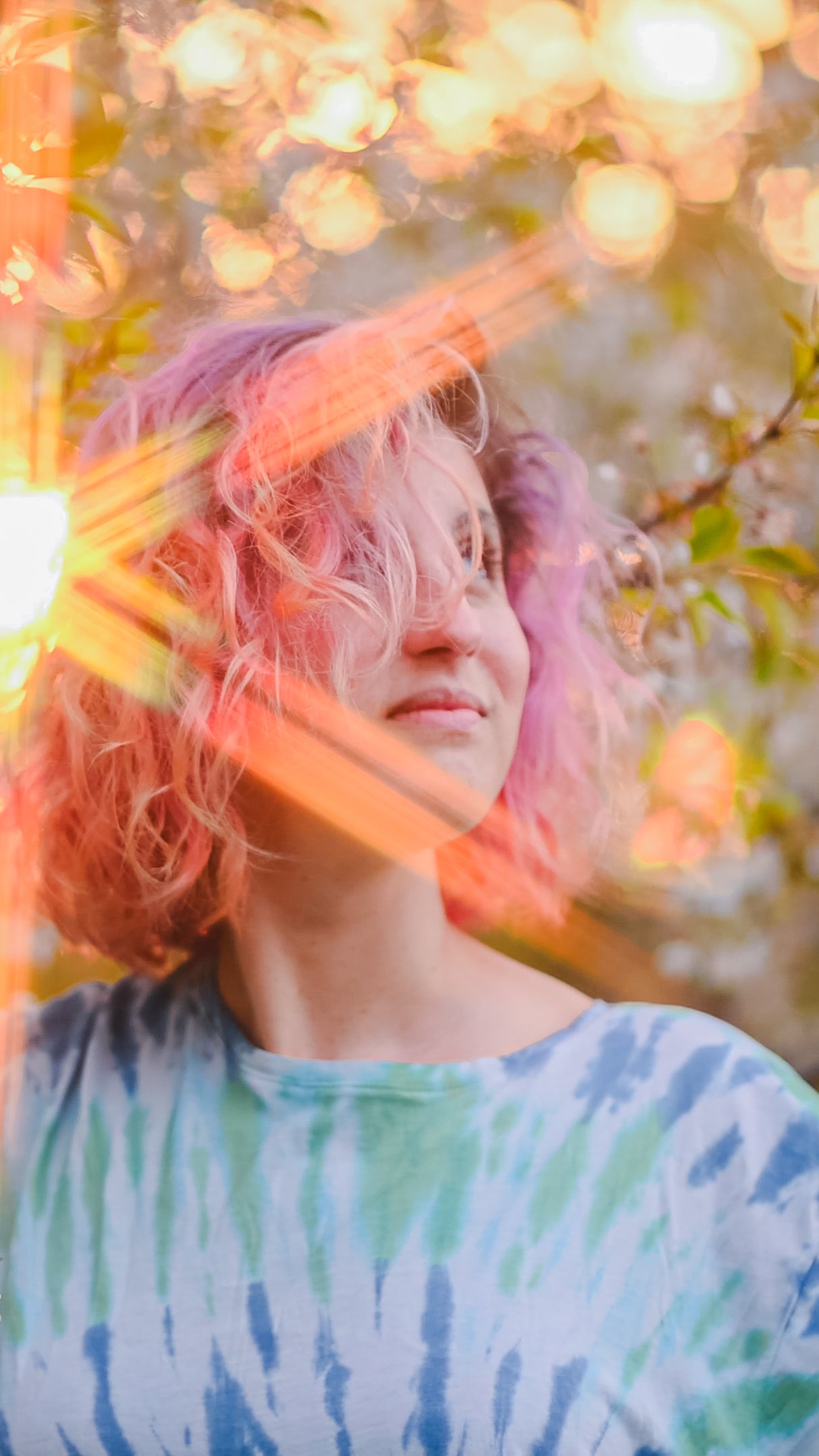 portrait of female with colourful hair looking off in distance with sun shinning through trees