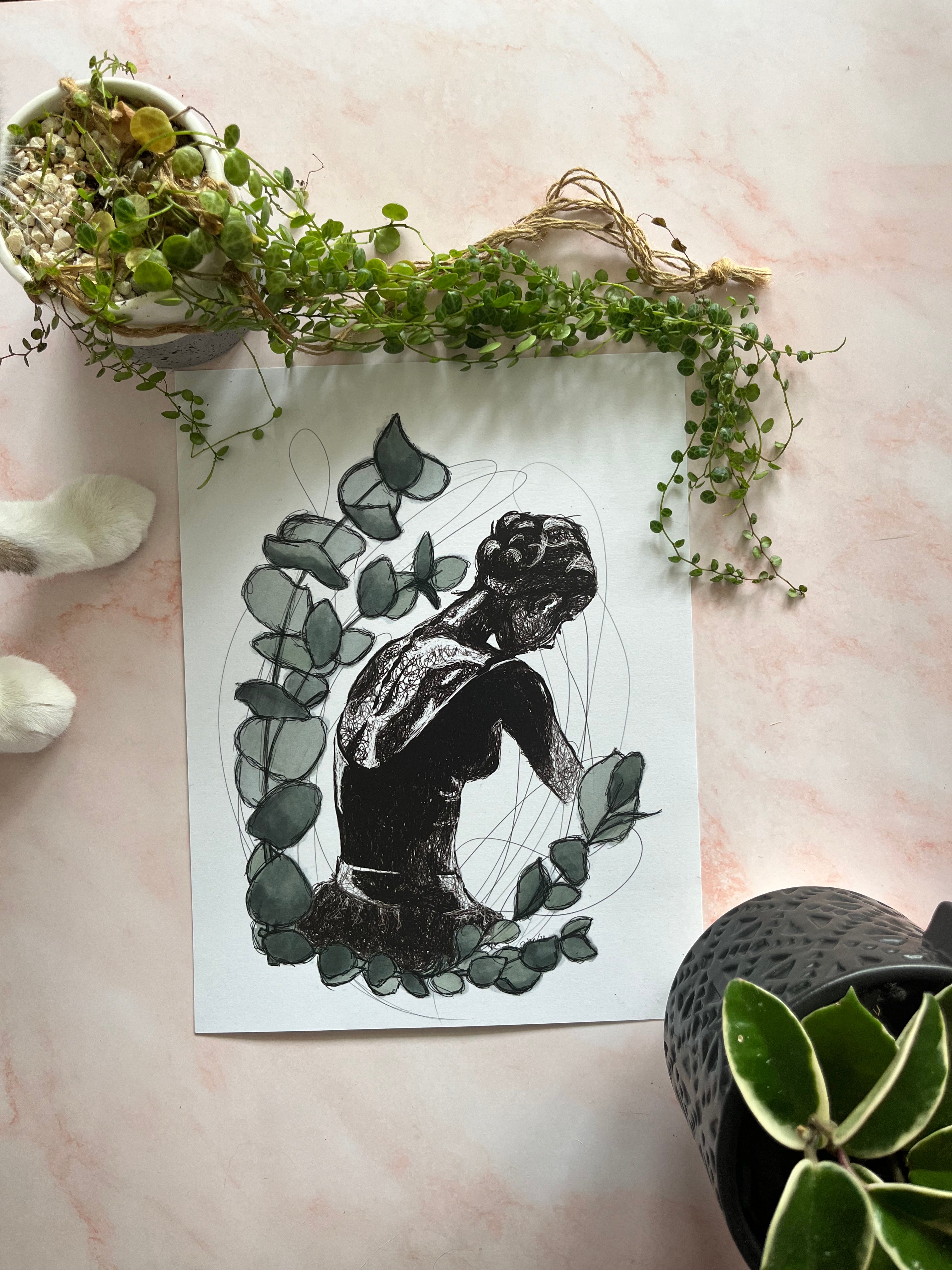 Picture of a fine art print of a female dancer's back. She is framed by sage coloured vines. The print has leafy plants that frame it and tiny cat paws off to the left